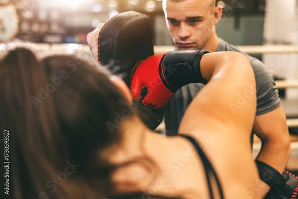 Fototapeta Boxing training session shows a woman practicing punches with a male trainer at a gym in the afternoon