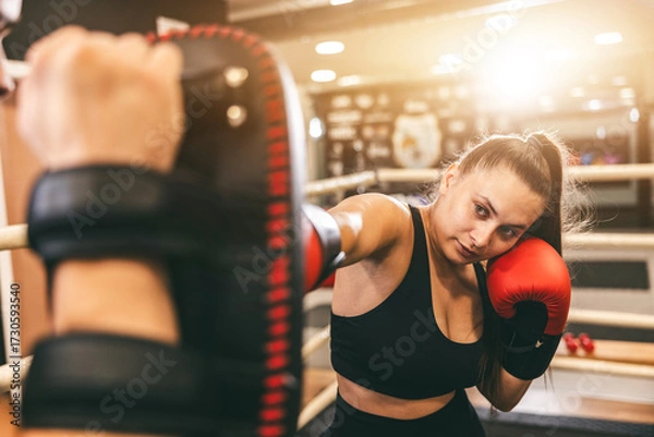 Fototapeta Female boxer training with focus mitts in a gym setting during daytime hours for skill development and strength building