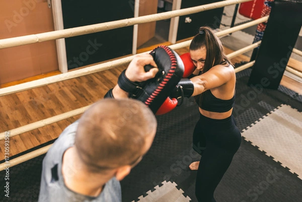 Fototapeta Female boxer practices punches while training with a coach in a gym setting during the day