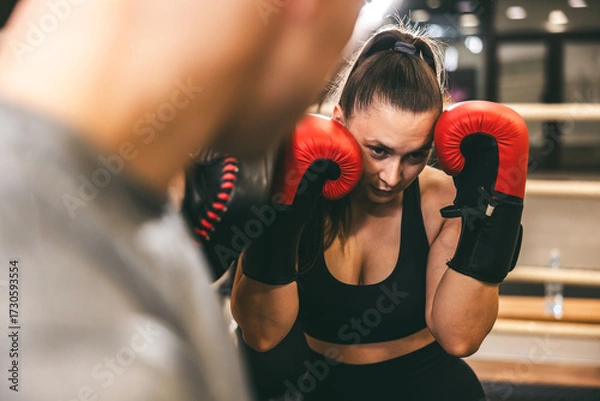 Fototapeta Woman practicing boxing techniques in a gym with a trainer observing her focus and form during a training session