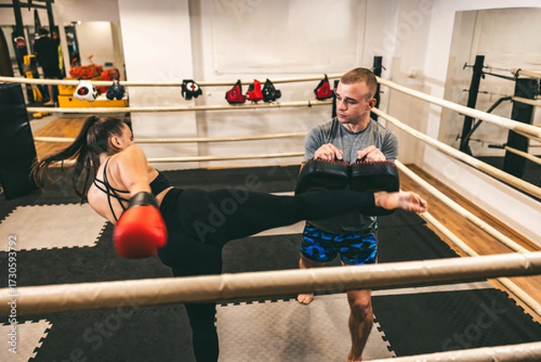 Fototapeta Training session at a martial arts gym featuring a kick and pad work between a coach and a student
