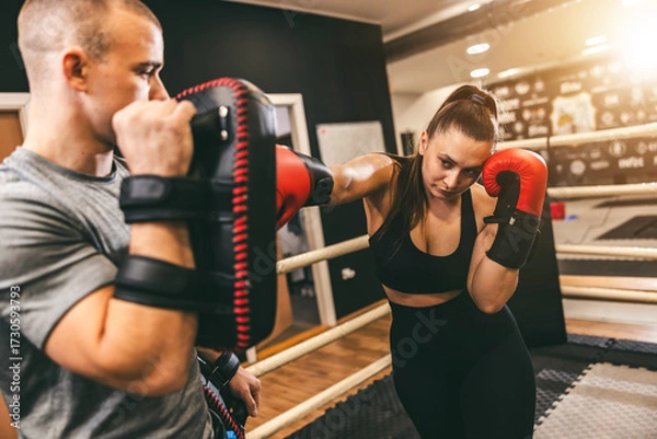 Fototapeta Female boxer practices punches with trainer in gym setting during afternoon training session