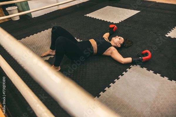 Fototapeta Boxing training session showing a woman resting on the mat after an intense workout in a gym during the afternoon