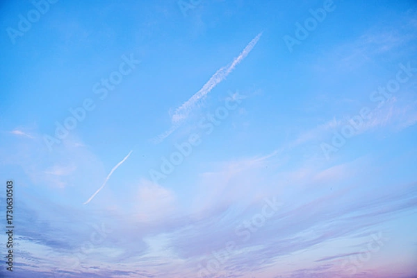 Fototapeta Clear blue sky with soft clouds and airplane contrails at sunset