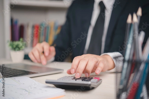 Obraz Accountant or financial analyst calculating data calculator in office. Professional working on business audit, company budget, and profit analysis with laptop and documents for investment planning.