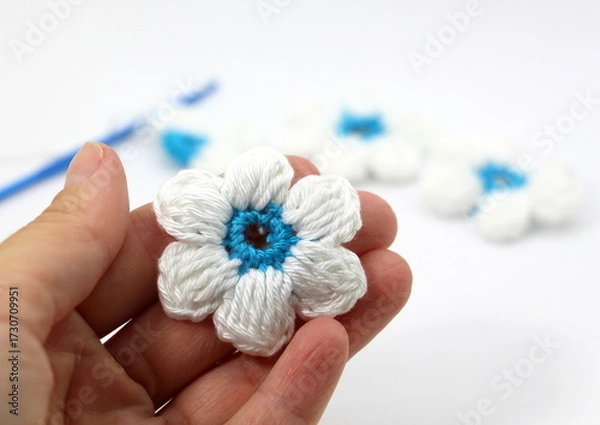 Fototapeta A flower with six white petals and a blue center crocheted on a white background.
