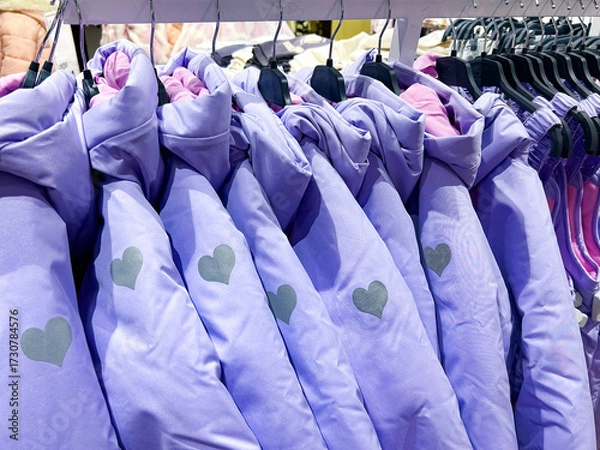Obraz  A row of purple jackets with heart patterns hangs neatly on hangers in a store. The jackets feature soft pink linings, displayed uniformly, evoking a sense of warmth and coziness.

