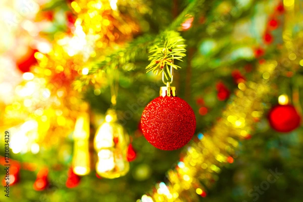 Fototapeta Christmas tree adorned with shiny lights in New Year. Bright Red Ornament Hanging on Christmas Tree With Colorful Decorations in Festive Setting. Vibrant red ball, ornament dangles on fir-tree.