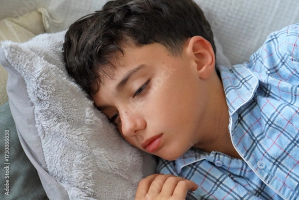 Fototapeta child health. Child in pajamas lying sick on the sofa with a look of discomfort or sadness.