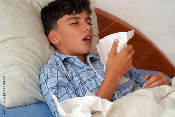 Fototapeta child in pajamas sick in bed with a cough and a tissue