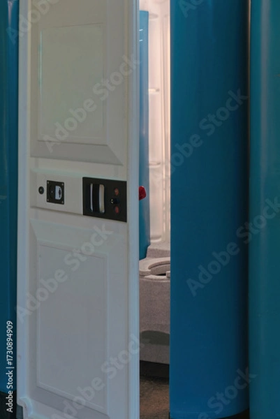 Fototapeta Portable toilet cabin with open door, showing the interior. Concept of outdoor sanitation, hygiene, and temporary facilities for public events or construction sites.