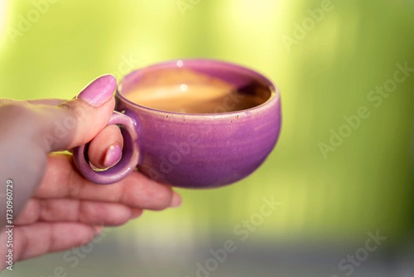 Fototapeta Espresso coffee in a small lilac mug. woman holding a ristretto on green background