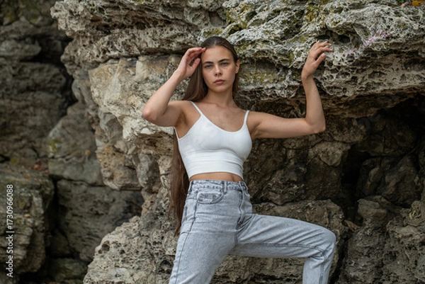 Obraz Beautiful woman in a white top and gray jeans poses on rocks in the mountains