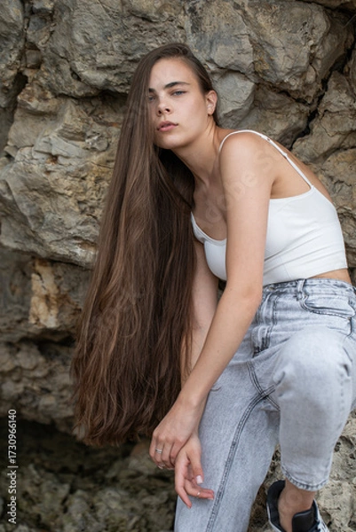 Obraz Beautiful woman in a white top and gray jeans poses on rocks in the mountains