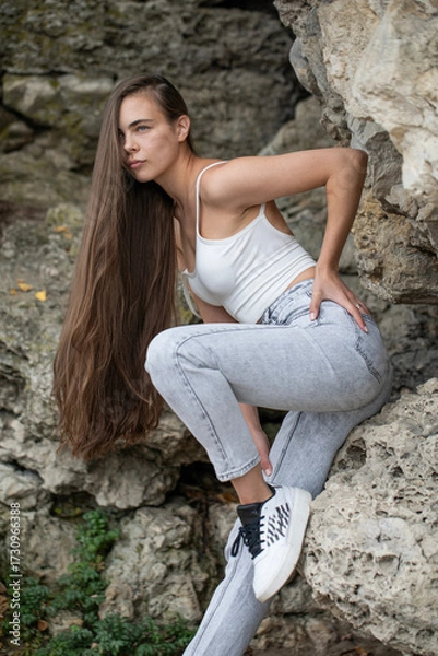 Obraz Beautiful woman in a white top and gray jeans poses on rocks in the mountains