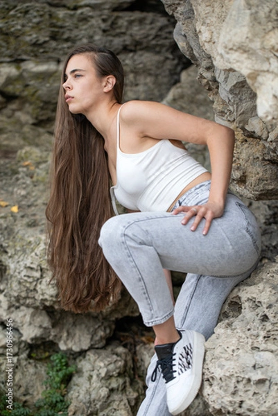 Obraz Beautiful woman in a white top and gray jeans poses on rocks in the mountains