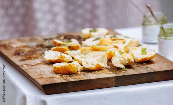 Fototapeta Sliced baguette on wooden cutting board with herb butter spread