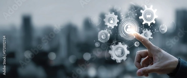 Fototapeta Hand interacting with digital gears and icons over a blurred cityscape