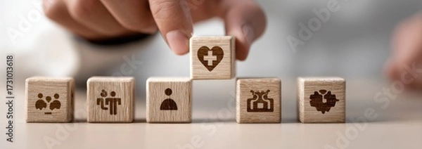 Fototapeta A hand places a wooden block with a heart and cross symbol on top of a stack of blocks with various icons