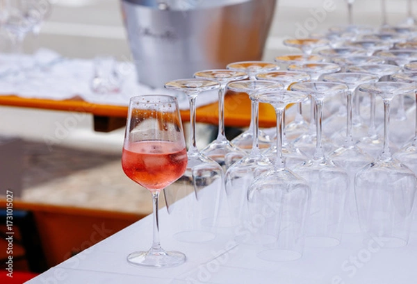 Fototapeta Elegant glass of rose wine stands out among a row of empty wine glasses on a table, showcasing a vibrant outdoor event atmosphere