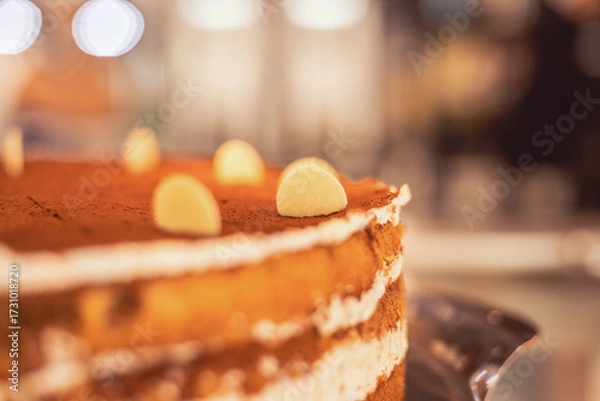 Fototapeta Layered cake with white chocolate highlights displayed in a cozy dessert shop during the evening