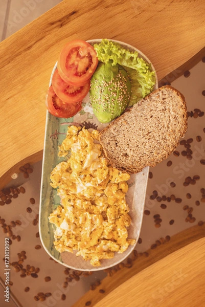 Fototapeta Delicious scrambled eggs with fresh vegetables and whole grain bread on a rustic wooden table