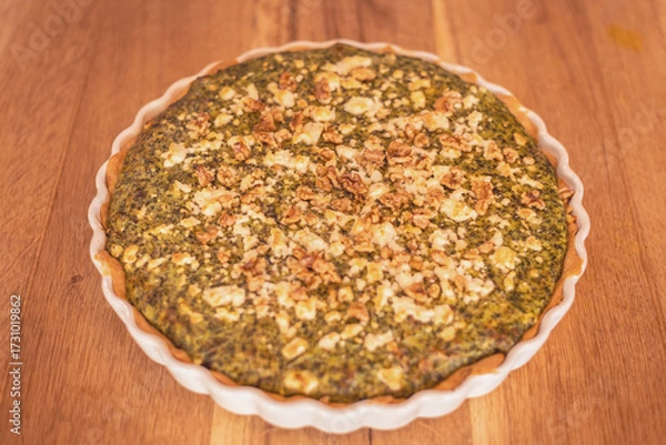 Fototapeta Savory herb tart topped with walnuts on a rustic wooden table perfect for family dinners