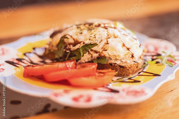 Fototapeta Savory breakfast open sandwich with tomatoes on a decorative plate in a cozy cafe setting