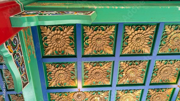 Fototapeta View upwards at a wooden pavilion roof with a repeating tile pattern and painted vibrant shades of gold, green, blue and red. 