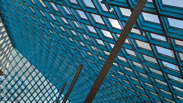 Fototapeta Low angle view of repeating pattern of windows along the large sloping surface of the roof with blue sky and sunlight visible. 