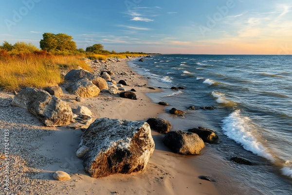 Obraz Rocky shoreline with waves washing onto sandy beach under a blue sky.
