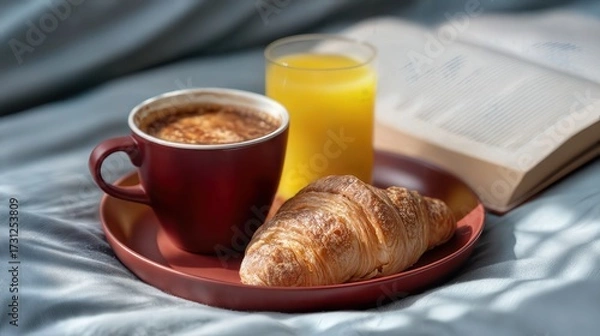 Fototapeta A cozy breakfast tray with coffee, orange juice, and a croissant beside a book on a bed, offering a perfect start to the day