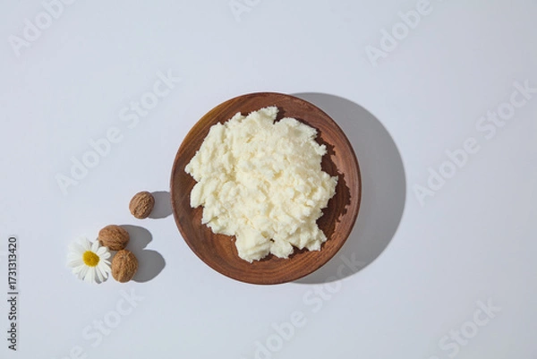 Fototapeta Top view of wooden bowl with raw shea butter, paired with chamomile flowers and nuts, minimalist concept for beauty and body care visuals.