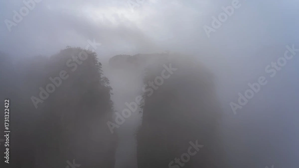 Fototapeta Mystical mountain landscape. The high sheer rock pillars  are shrouded in thick fog. Peaks in the clouds. A foggy morning. Poor visibility. China. Zhangjiajie National Forest Park. Avatar