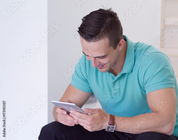 Fototapeta man using a tablet while sitting on the stairs at home