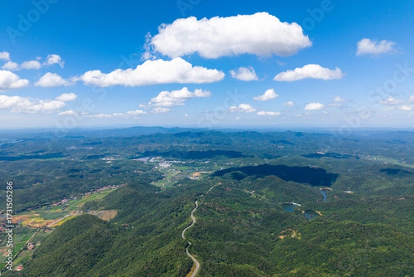 Fototapeta Dahong Mountain rises majestically under a blue sky with white clouds, showcasing lush green landscapes and rolling hills stretching across Suizhou, China.