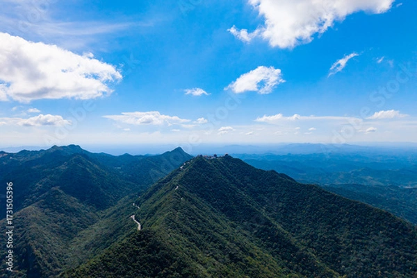 Fototapeta Dahong Mountain rises under a blue sky with clouds, presenting vast green valleys and a winding path reaching toward the distant horizon.