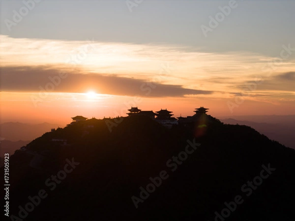 Fototapeta Dahong Mountain silhouette against a sunset sky in Suizhou, China, with buildings crowning the peak and the sun low on the horizon.