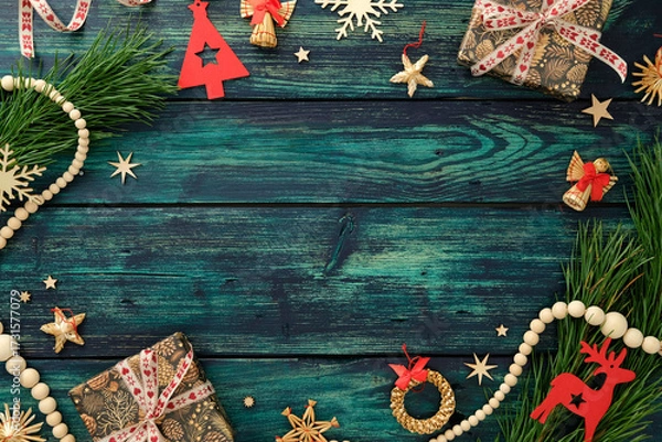 Fototapeta Rustic Christmas flat lay with gifts, pine branches, festive ornaments, and wooden beads on teal wood table