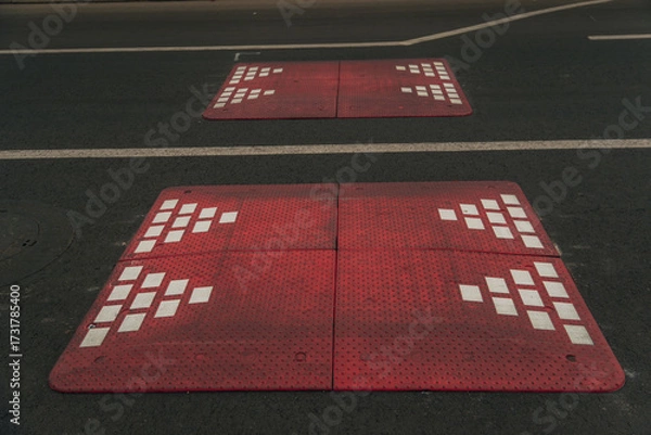 Fototapeta Modular speed bumps (speed bumps) of red color with white reflective elements, installed on an asphalt road in a residential area or on the outskirts of the city.