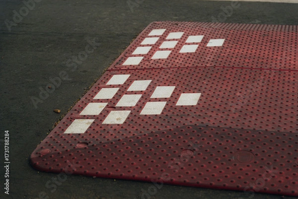 Fototapeta Modular speed bumps (speed bumps) of red color with white reflective elements, installed on an asphalt road in a residential area or on the outskirts of the city.