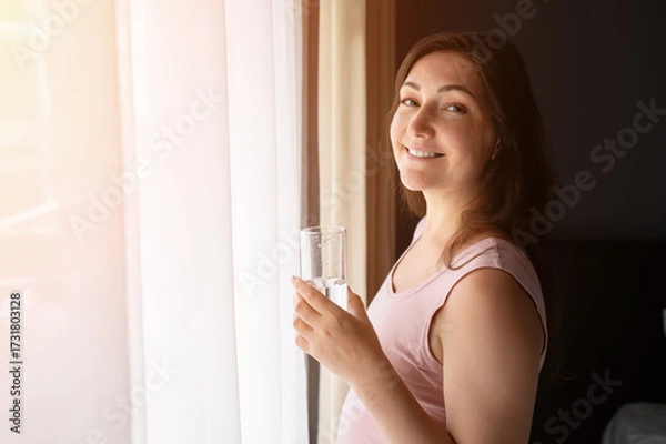 Obraz Pregnant woman drinking water and smiling by the window