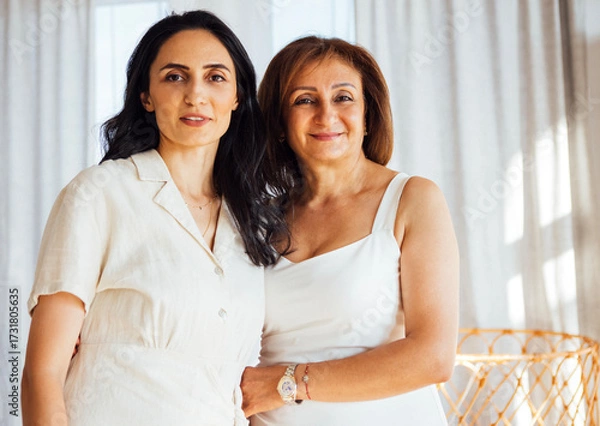 Fototapeta Two women, one in a light dress and the other in a casual outfit, stand together in a bright, airy room, showcasing warmth and connection in a modern interior setting