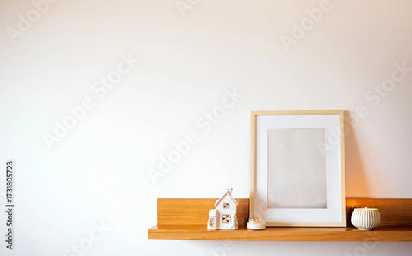 Fototapeta Minimalist shelf display featuring a blank picture frame, decorative ceramic house, and a candle, creating a serene and stylish home decor atmosphere with copy space