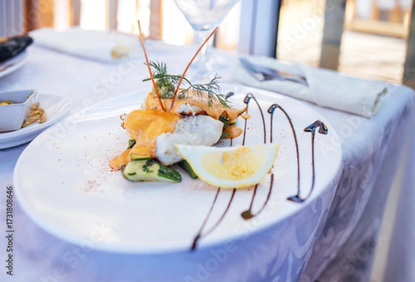 Fototapeta Gourmet seafood dish elegantly plated with grilled fish, fresh vegetables, and lemon slice, garnished with herbs, showcasing culinary artistry and fine dining experience