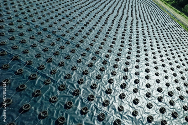 Fototapeta A geomembrane landfill cover secured with tires and ropes in a structured grid pattern, designed to contain waste, prevent contamination, and protect the environment