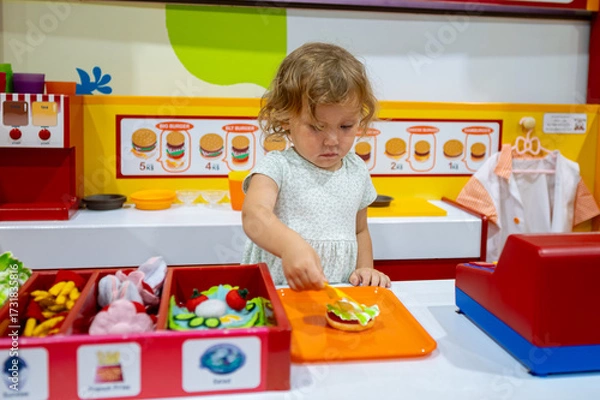 Obraz Little girl playing cook preparing toy hamburger in playroom