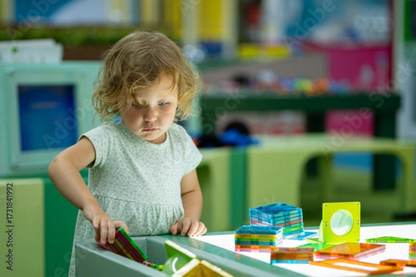 Obraz Cute toddler girl playing with colorful magnetic tiles on light table in playroom