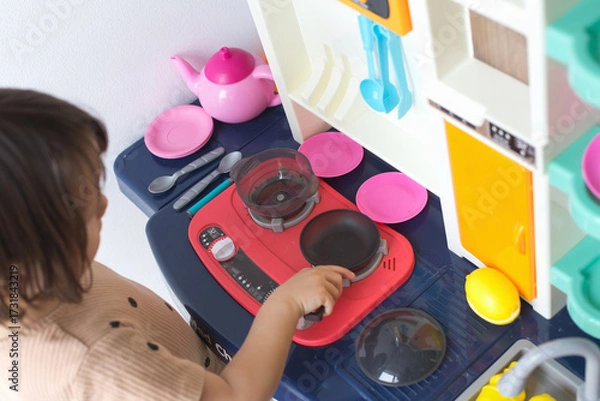 Fototapeta Child playing at toy kitchen stove with utensils, plates and cookware, engaging in imaginative pretend cooking activity, concept of childhood