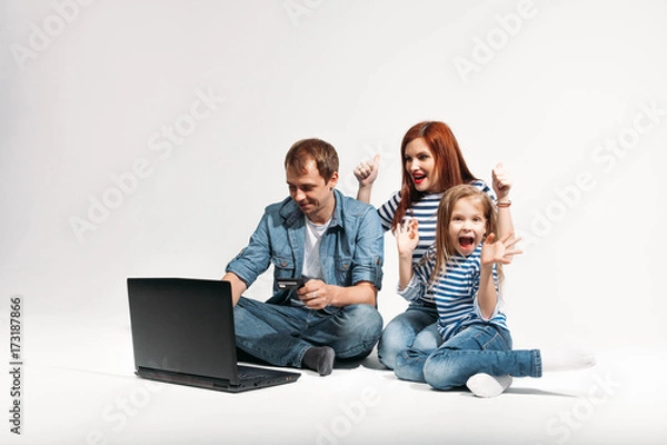 Fototapeta Happy family Father, mother and child lying on the floor with laptop credit card on white background isolated
